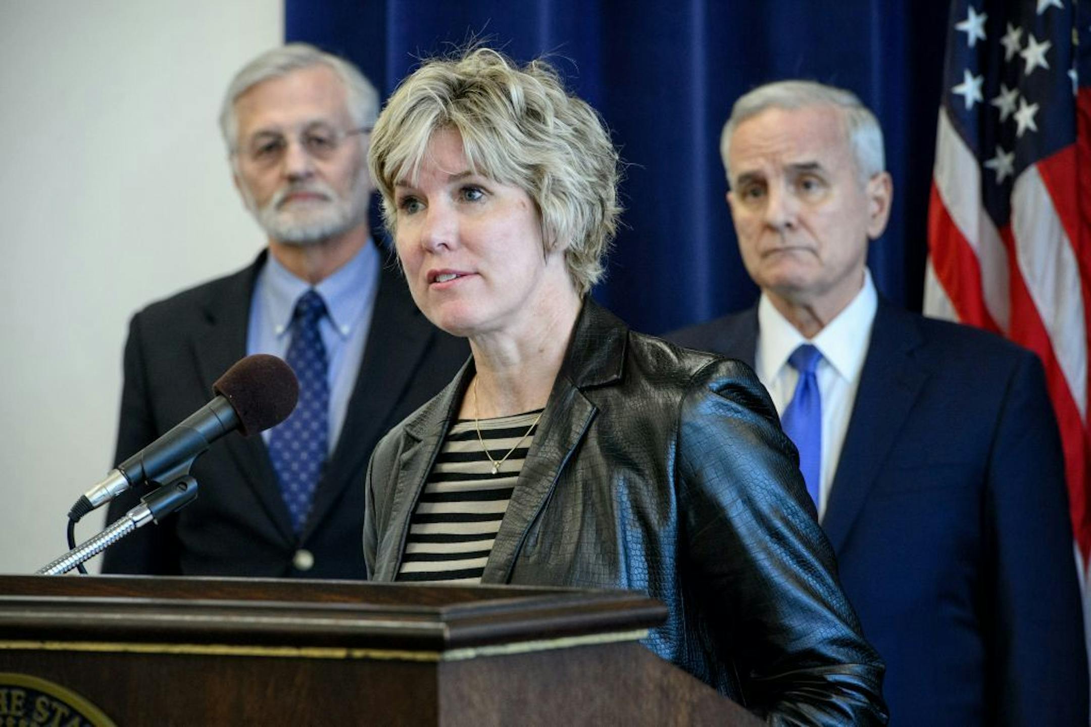 At the podium Kris Ehresmann, Director, Infectious Disease, Epidemiology and Control, Minnesota Department of Health behind her Kris Ehresmann, Director, Infectious Disease, Epidemiology and Control, Minnesota Department of Health and Governor Mark Dayton.