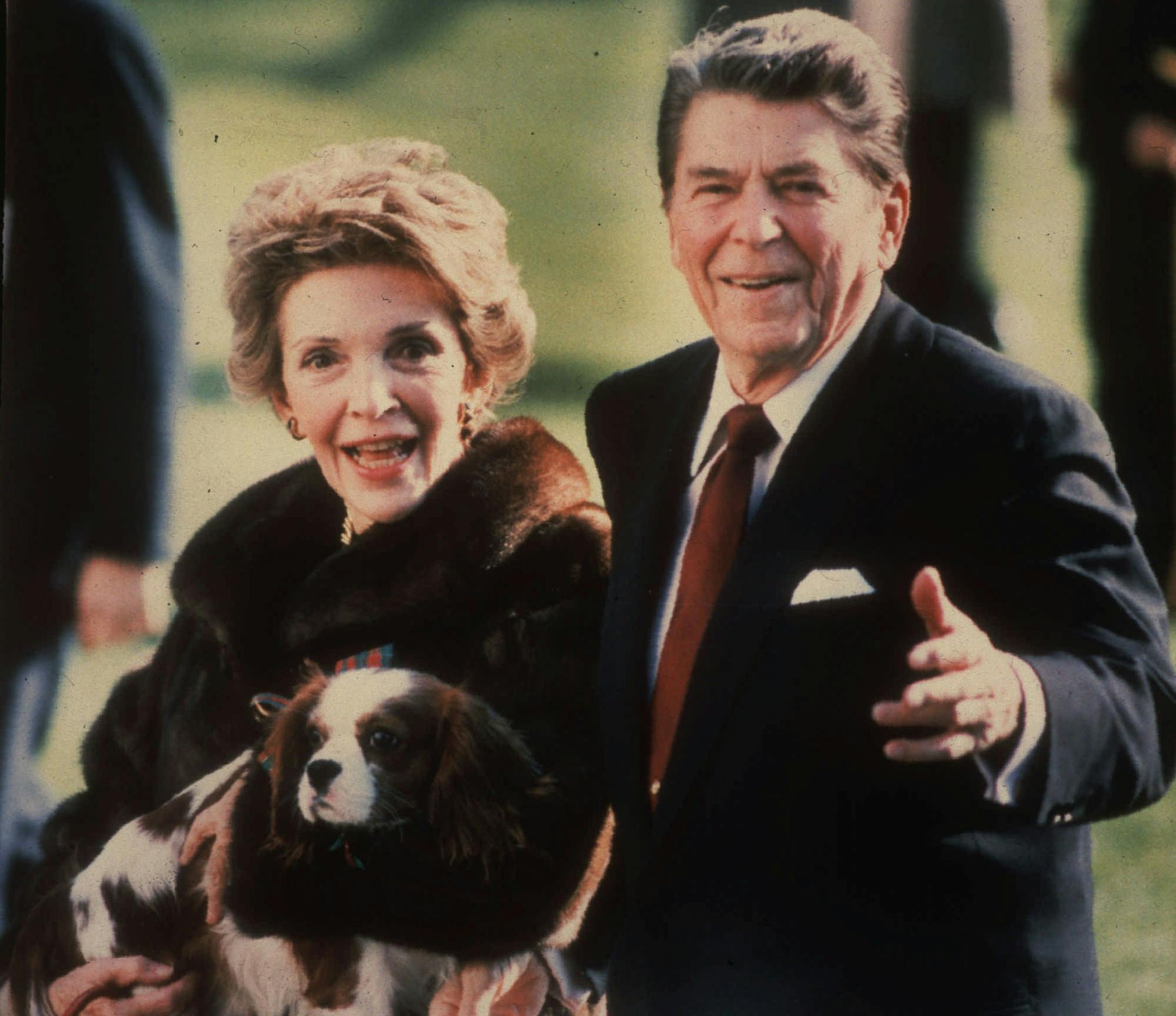 December 1986: Nancy Reagan cradles the Reagans' pet, a King Charles spaniel named Rex, as she and President Reagan stroll along the White House South lawn.