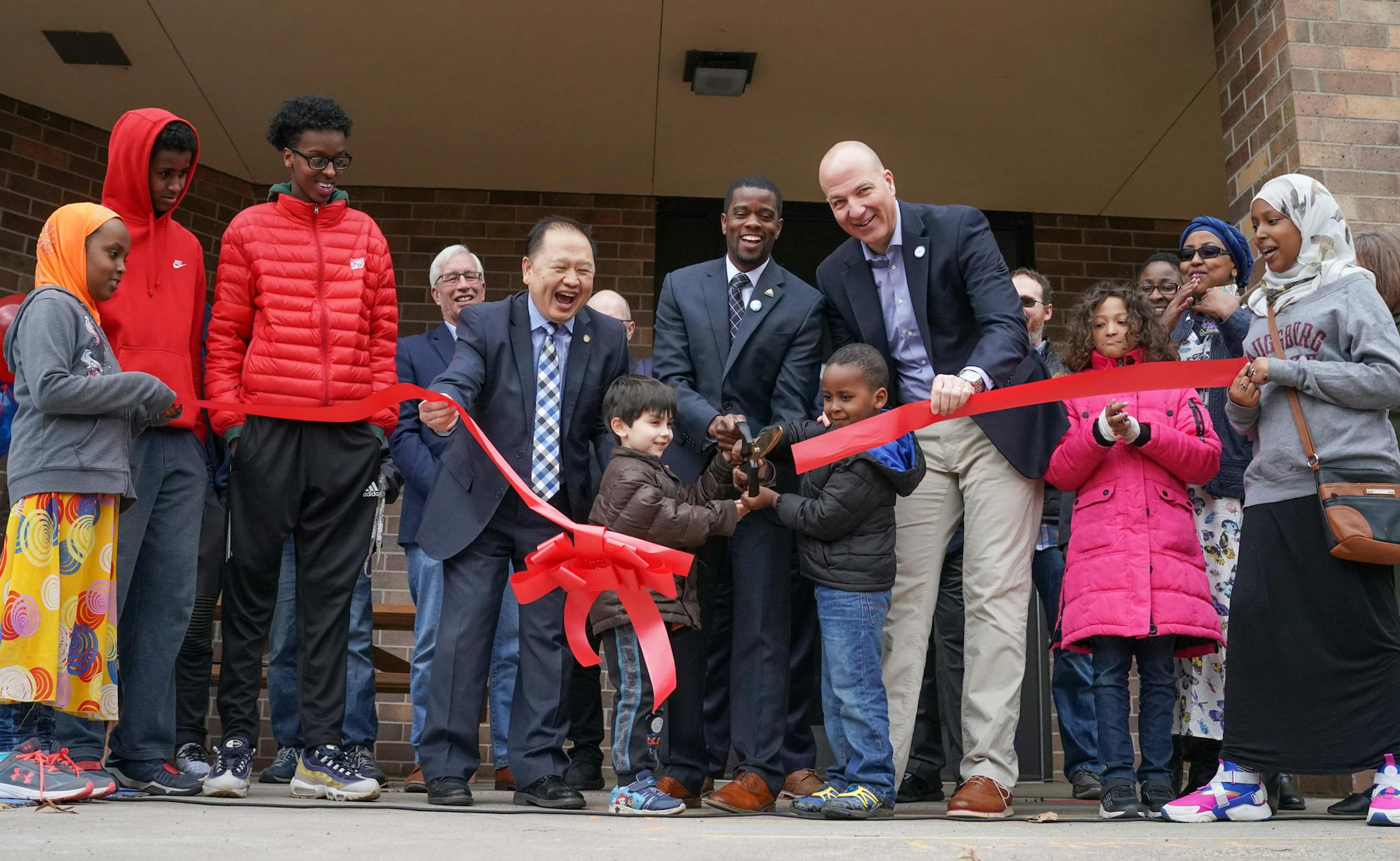 Mayor Melvin Carter called on all the neighborhood kids at the grand opening to cut the big ribbon with the big scissors. On the left, Senator Foung Hawj, on the right, St Paul School Superintendent Joe Gothard.