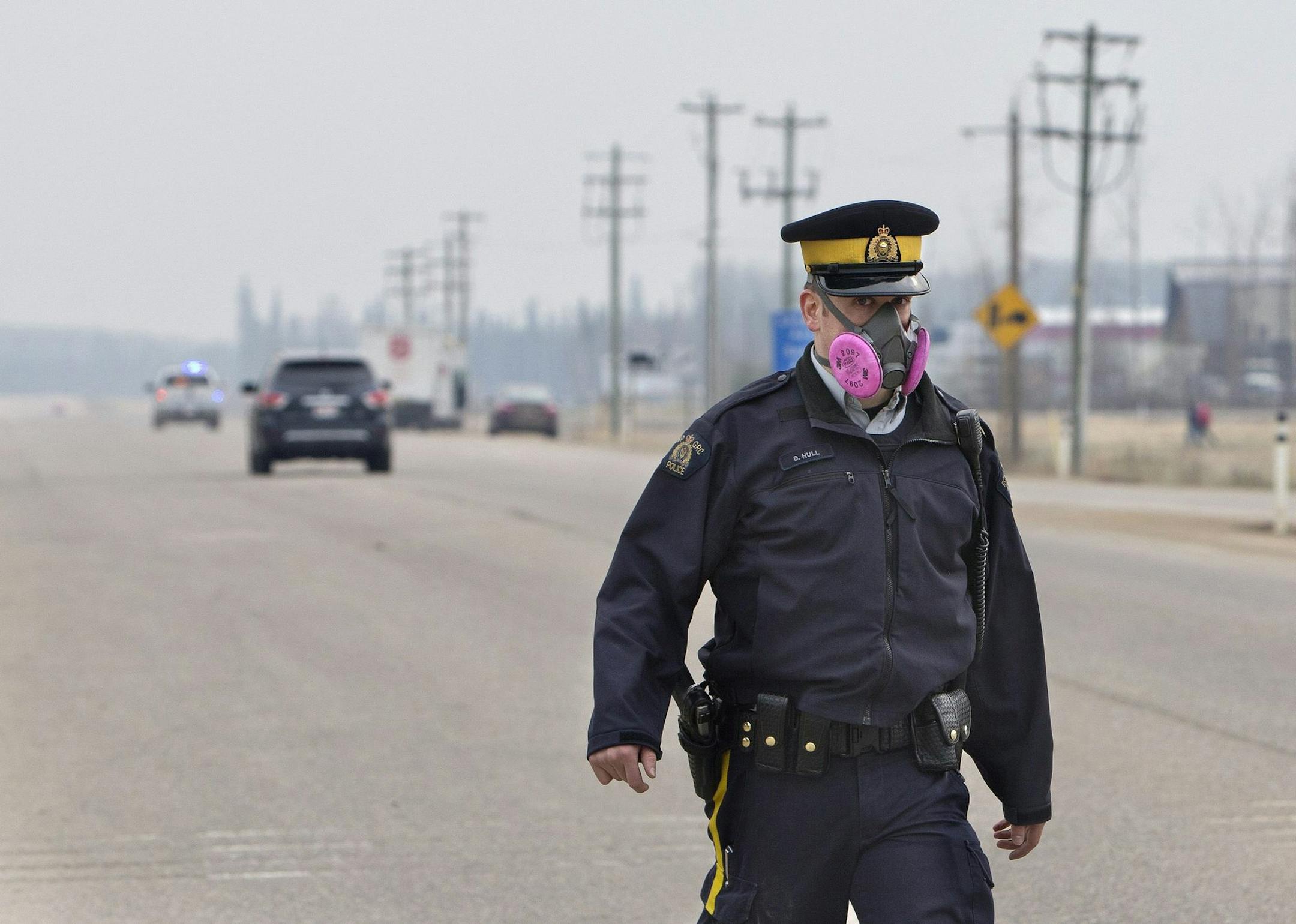 A police officer wears a mask while controlling a roadblock near a wildfire in Fort McMurray, Alberta, Canada on Thursday, May 5, 2016. Raging wildfires in the Canadian province of Alberta have moved south, forcing three more communities to evacuate and an emergency operations center to move again , aking it far from the devastated oil sands city of Fort McMurray. (Jason Franson/The Canadian Press via AP) MANDATORY CREDIT