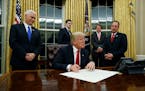 Vice President Mike Pence watches at left as President Donald Trump prepares to sign his first executive order, Friday, Jan. 20, 2017, in the Oval Off