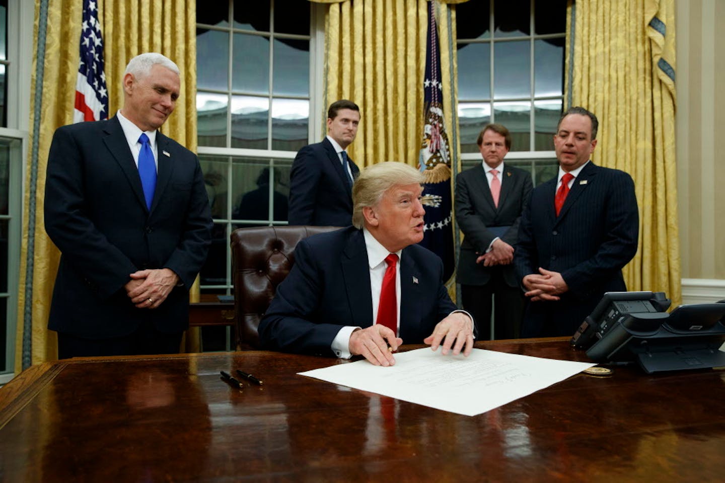 Vice President Mike Pence watches at left as President Donald Trump prepares to sign his first executive order, Friday, Jan. 20, 2017, in the Oval Office of the White House in Washington.