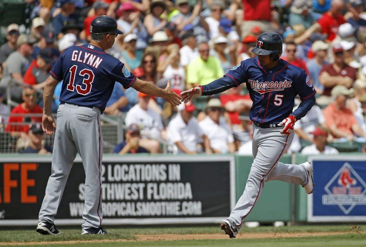 Minnesota Twins third base coach Gene Glynn, left, greets Eduardo Escobar as he rounds the bases after hitting a solo home run in the second inning of a spring training baseball game against the Boston Red Sox in Fort Myers, Fla., Thursday, March 10, 2016.