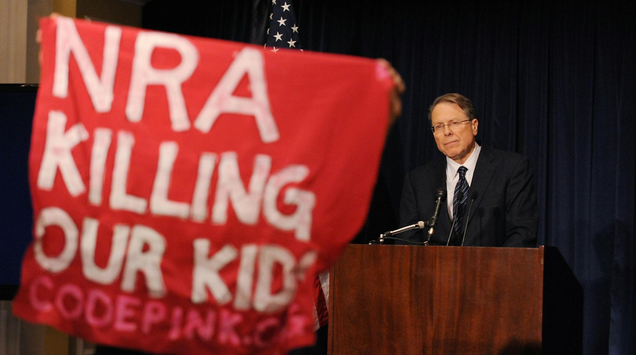 A protester holds up a sign as Wayne LaPierre, executive vice-president of the National Rifle Association of America (NRA), speaks at a news conference at the Willard Hotel, December 21, 2012 in Washington, DC. The nation's largest gun lobby called Friday for Congress to require armed security guards in every school, saying it would help prevent such acts of mass violence from happening again.