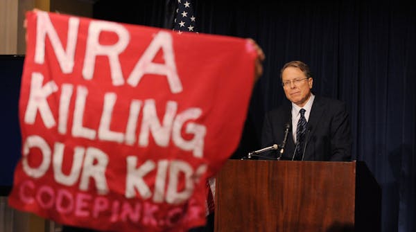 A protester holds up a sign as Wayne LaPierre, executive vice-president of the National Rifle Association of America (NRA), speaks at a news conferenc