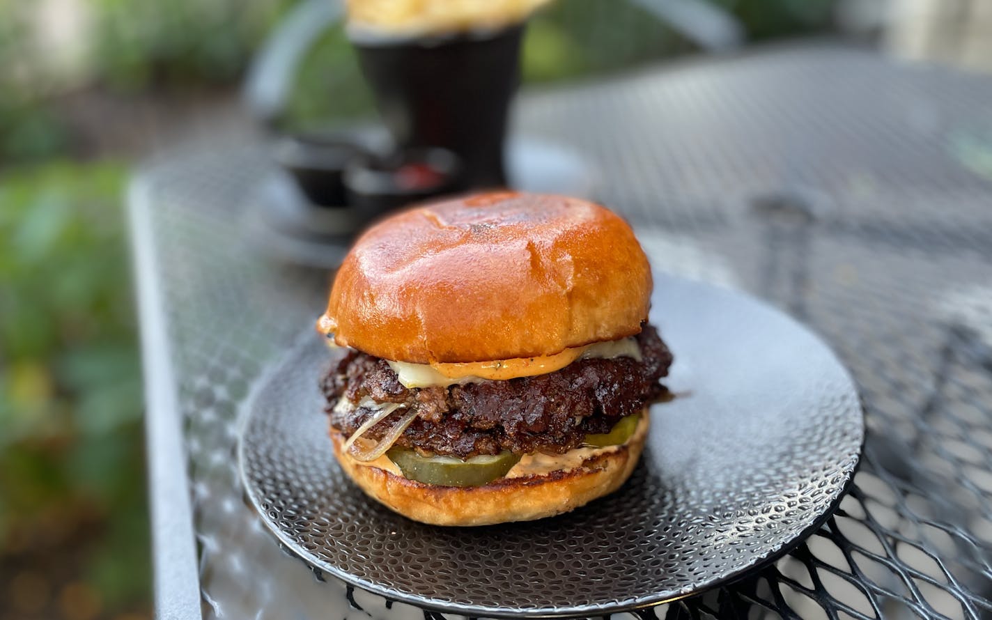 A double stacked smash burger is layered with caramelized onion slices and one thick pickle sticking out of the bottom of the bun. Burger sauce oozes out just a little bit at the top and bottom of the burger. The brioche bun has just a hint of toasting on the top.