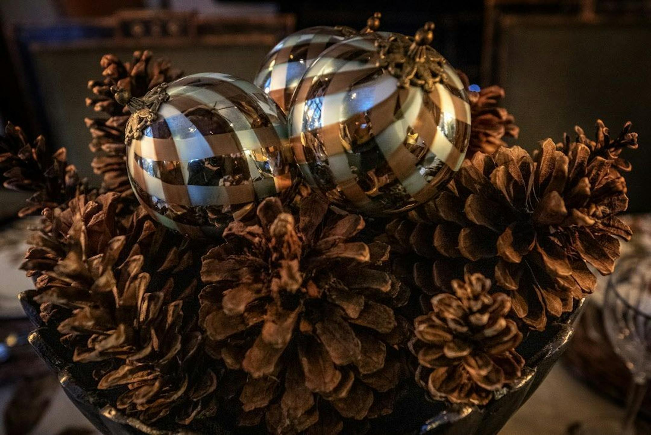 The simple dining table centerpiece is composed of jumbo pine cones and blue-gold-silver ball ornaments inside a pewter bowl.