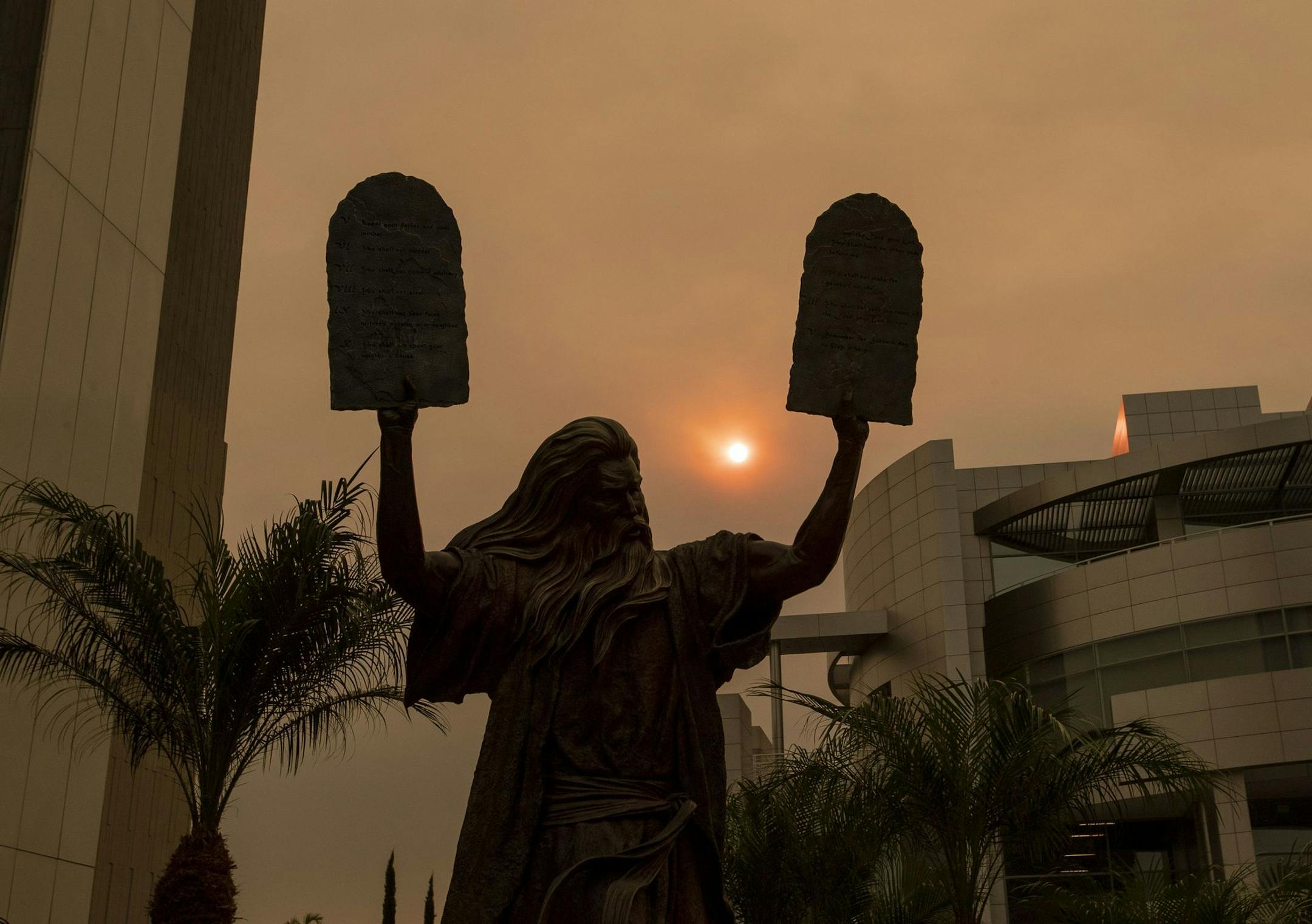 GARDEN GROVE, CA - SEPTEMBER 09: The sun and a bronze statue of Moses putting the ten commandments of two tables in the air are partially obscured with ash from Southland wildfires at the Christ Cathedral in Garden Grove Wednesday, Sept. 9, 2020. With so many fires burning, millions of people in the Bay Area, Central Valley and parts of Southern California are breathing dangerous levels of particle pollution. (Allen J. Schaben / Los Angeles Times/TNS) ORG XMIT: 1766895