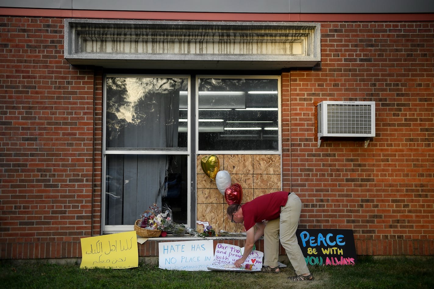 Ben Sunderlin placed a sign of support near the window that was damaged during Saturday morning's attack at the Dar Al Farooq Islamic Center in Bloomington.