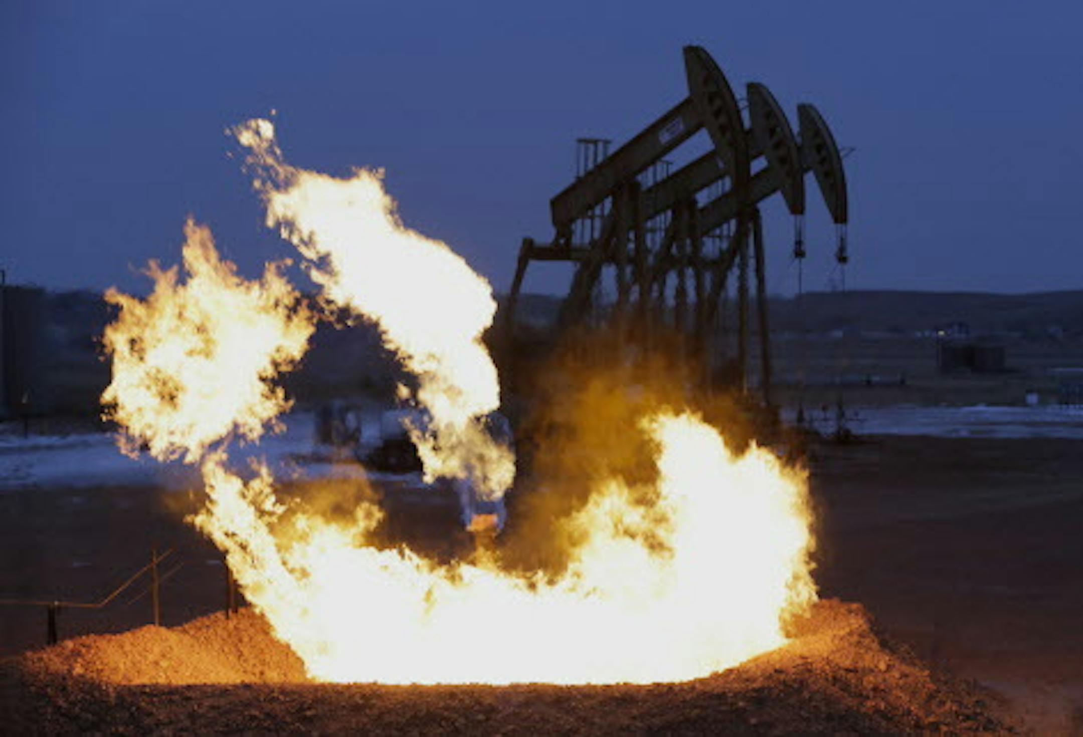 In this Wednesday, Dec. 17, 2014 photo, flames erupt from a natural gas flare near oil pump jacks in the Watford City, N.D. area. The gusher of oil and money flowing from the Bakken fields have made policing more demanding and dangerous, forcing small-town officers, county sheriffs and federal agents to confront everything from rowdy bar fights to far-reaching methamphetamine and heroin networks and prostitution rings operating out of local motels. (AP Photo/Eric Gay)