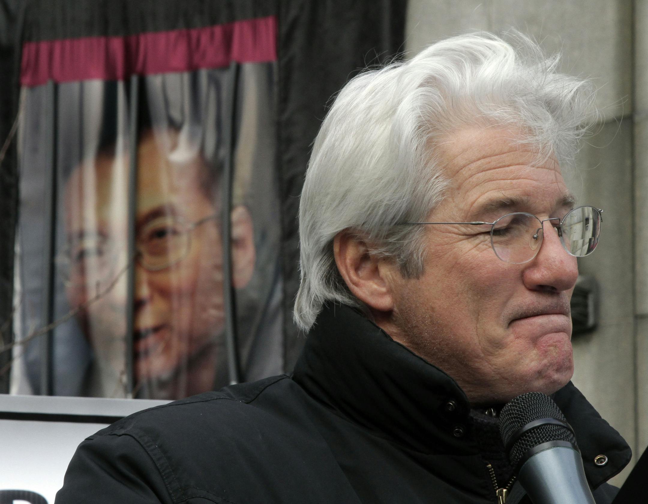 Actor Richard Gere pauses during a rally for Nobel Peace Prize recipient Liu Xiaobo, whose portrait hangs at background left, across from the United Nations, in New York, Friday, Dec. 10, 2010. (AP Photo/Richard Drew) ORG XMIT: NYRD104