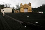 A woman stands near a church as the ground is covered in volcanic ash in Calderas, Guatemala, Friday May 28, 2010 after the Pacaya Volcano erupted a d