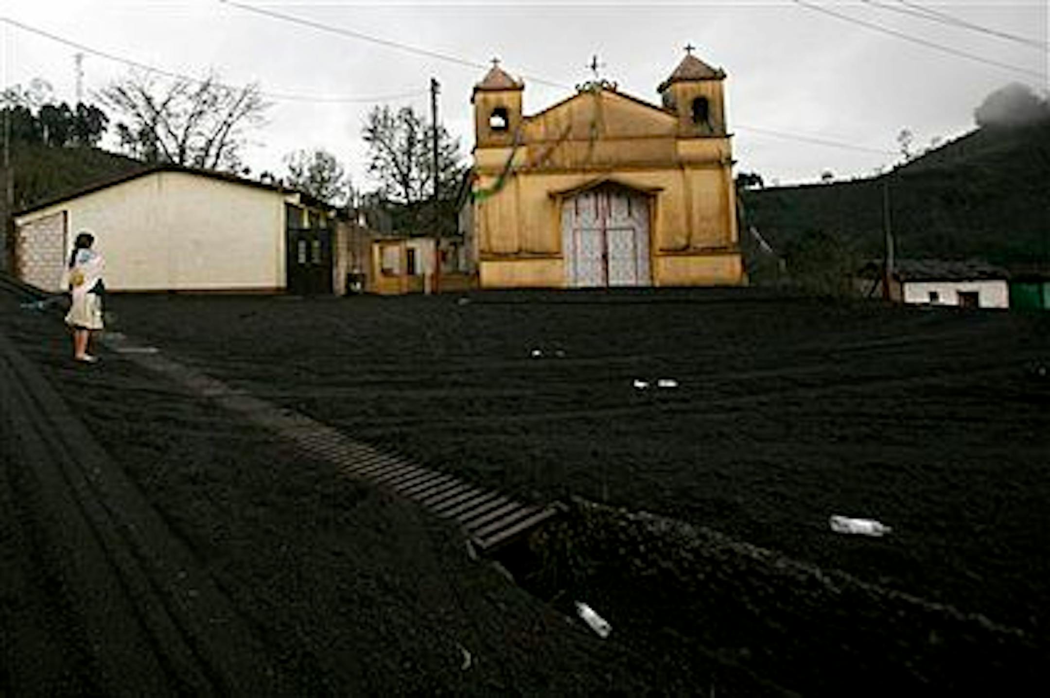 A woman stands near a church as the ground is covered in volcanic ash in Calderas, Guatemala, Friday May 28, 2010 after the Pacaya Volcano erupted a day earlier. The volcano started erupting lava and rocks on Thursday afternoon, blanketing Guatemala City with ash and forcing the closure of the international airport. One television reporter has been killed and thousands of residents from villages closest to the volcano have been evacuated to shelters.  (AP Photo/Moises Castillo)