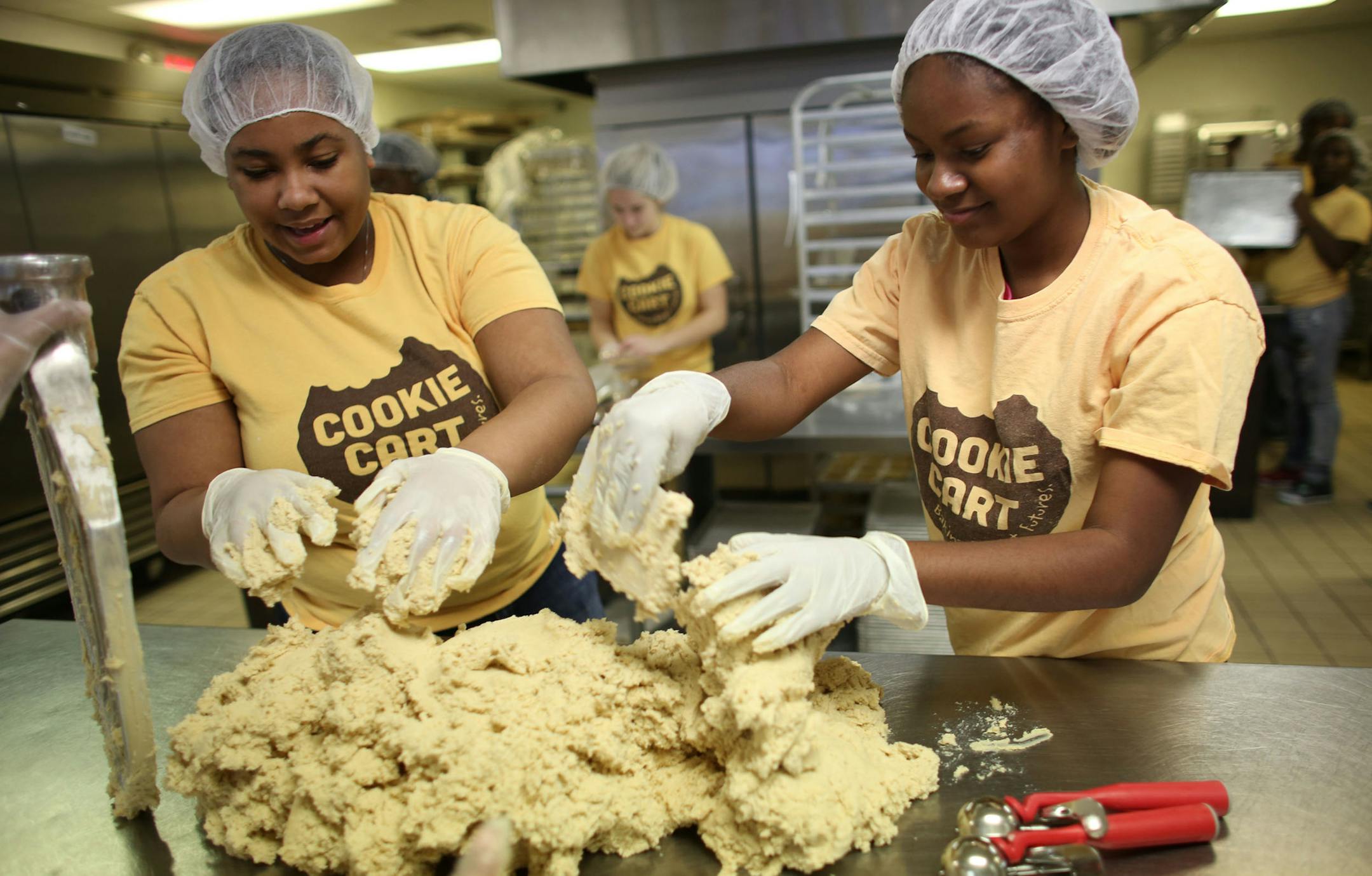 Summer Davis, left, 17, Diamond Lloyd, 15, piled on the cookie dough as they prepared to make M&M cookies with some of the 145 teens who work at the Cookie Cart in north Minneapolis.