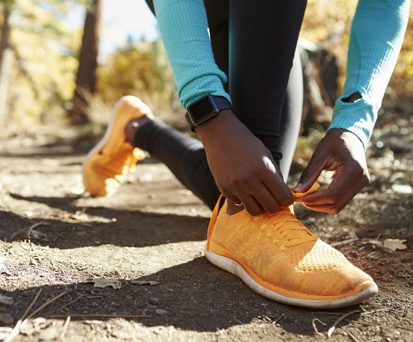 Black female runner in forest tying shoe, low section detail