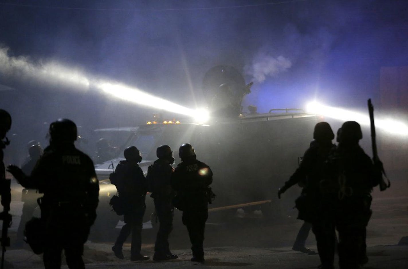 Police in riot gear stand around an armored vehicle as smoke fills the streets Tuesday, Nov. 25, 2014, in Ferguson, Mo. Missouri's governor ordered hundreds more state militia into Ferguson on Tuesday, after a night of protests and rioting over a grand jury's decision not to indict police officer Darren Wilson in the fatal shooting of Michael Brown, a case that has inflamed racial tensions in the U.S.