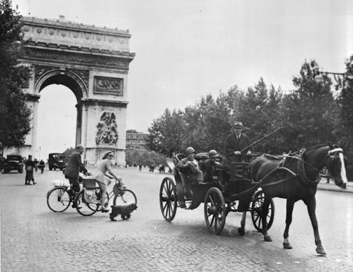 photo of a horse and carriage, people on bicycles and the Arc de Triomphe