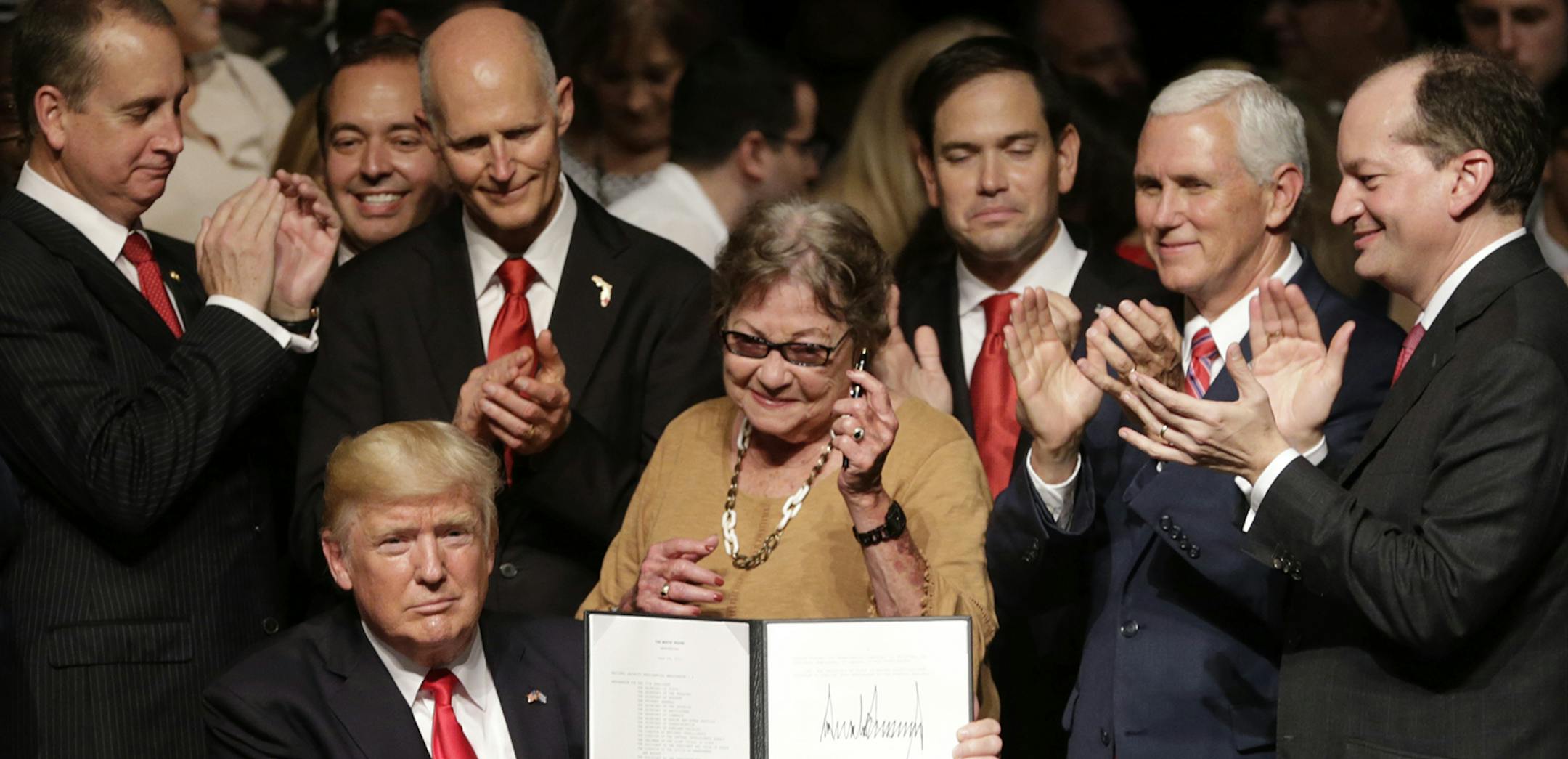 President Donald Trump signs an executive order on a revised Cuba policy aimed at stopping the flow of U.S. cash to the country's military and security services while maintaining diplomatic relations, Friday, June 16, 2017, in Miami. From left are, Agriculture Secretary Sonny Perdue, Commerce Secretary Wilbur Ross, Rep. Mario Diaz-Balart, R-Fla., Florida Gov. Rick Scott, Cary Roque, Senator Marco Rubio, R-Fla., Vice President Mike Pence and Labor Secretary Alex Acosta. (AP Photo/Lynne Sladky) OR