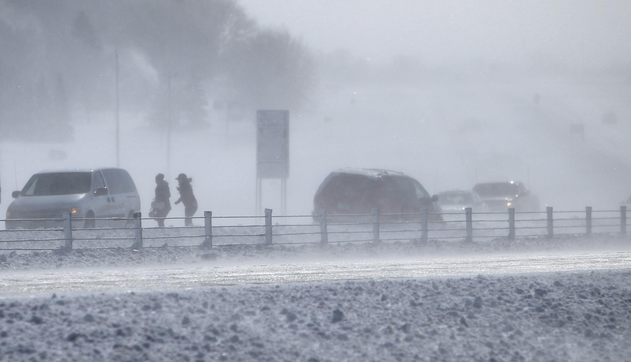 Blizzard-like conditions near along I-35 Friday, Feb. 21, 2014, MN. I-35 to the south at Owatonna, MN into Iowa because of blizzard conditions. Here, two people stand along the I-35 roadside after one vehicle lost control and spun around and wound up in the ditch facing the wrong direction north of Owatonna, MN.