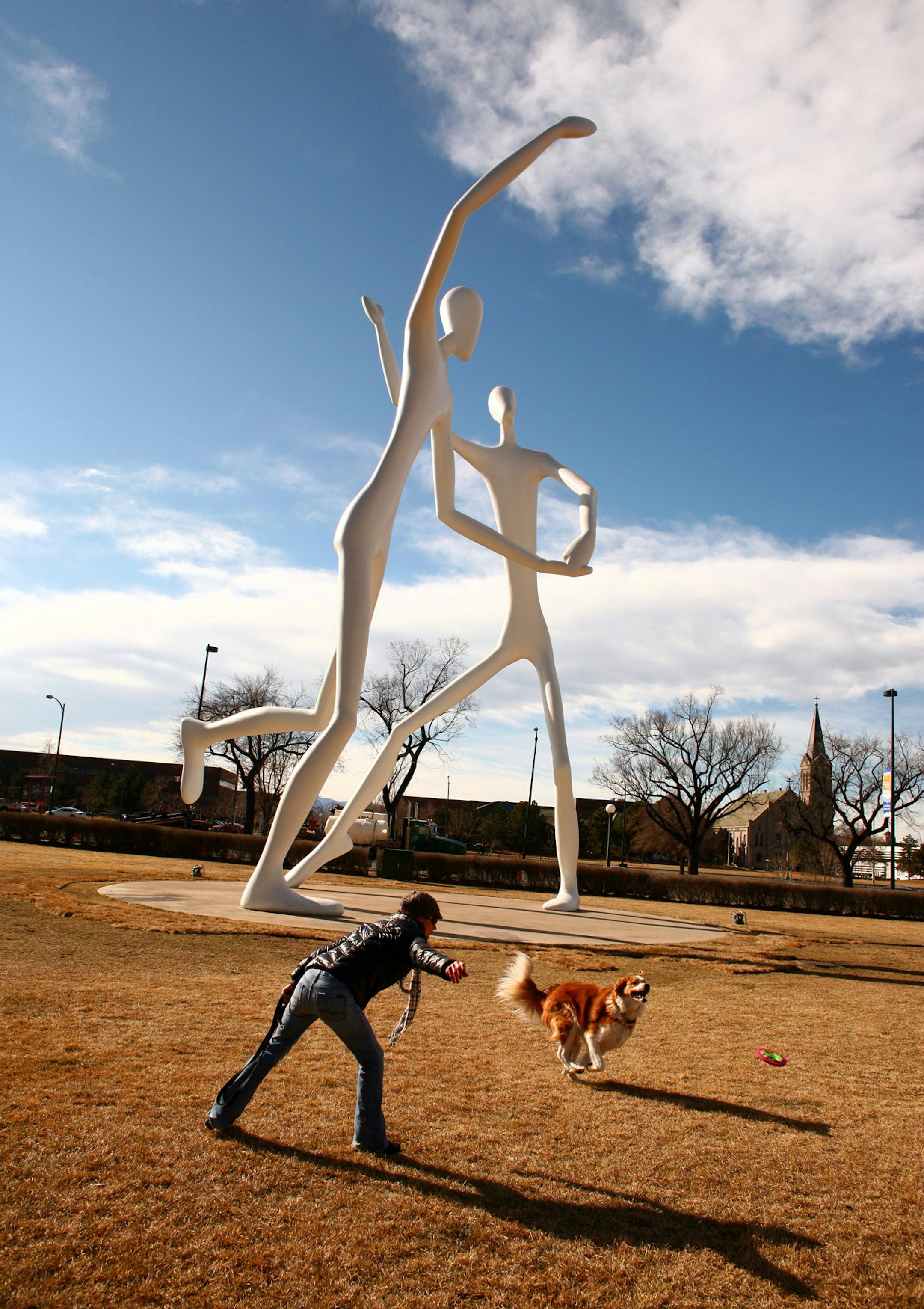 A woman plays with her dog near a sculpture called Dancers by Jonathan Borofsky, outside the Denver Performing Arts Complex. Denverís restaurant scene, art galleries, bars and nightclubs draw young professionals. Illustrates DENVER (category f) by Nadja Brandt (c) 2013, Bloomberg News. Moved: Tuesday, Dec. 31, 2013 (MUST CREDIT: Bloomberg News photo by Matthew Staver).