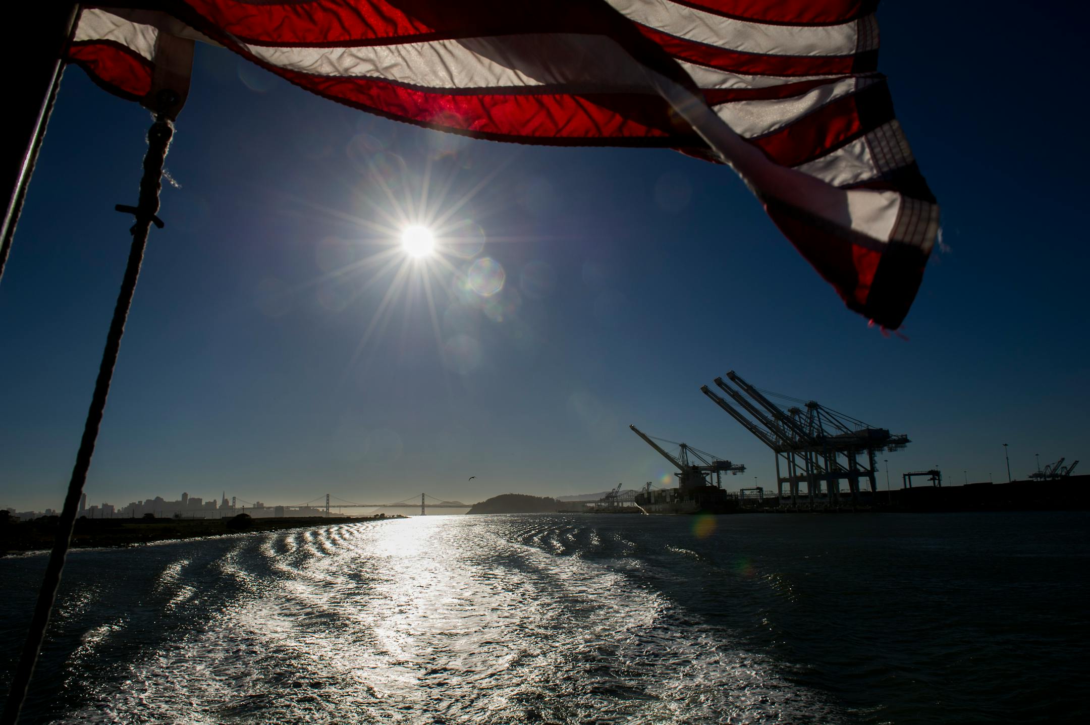 A U.S. flag flies as cranes stand at the Port of Oakland in Oakland, California, U.S., on Thursday, June 20, 2013. The U.S. Commerce Department's Bureau of Economic Analysis is scheduled to release gross domestic product (GDP) figures on June 26. Photographer: David Paul Morris/Bloomberg