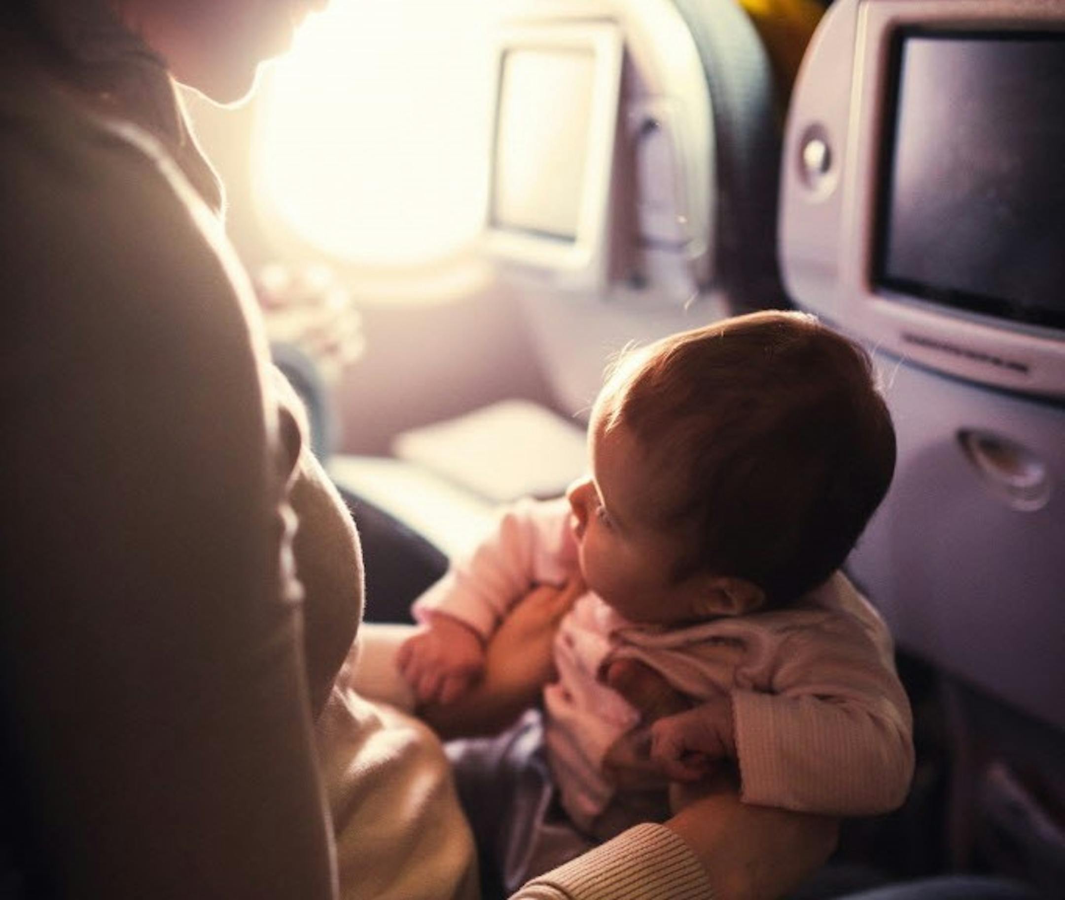 A mother and her baby girl sit in a passenger airline seat.