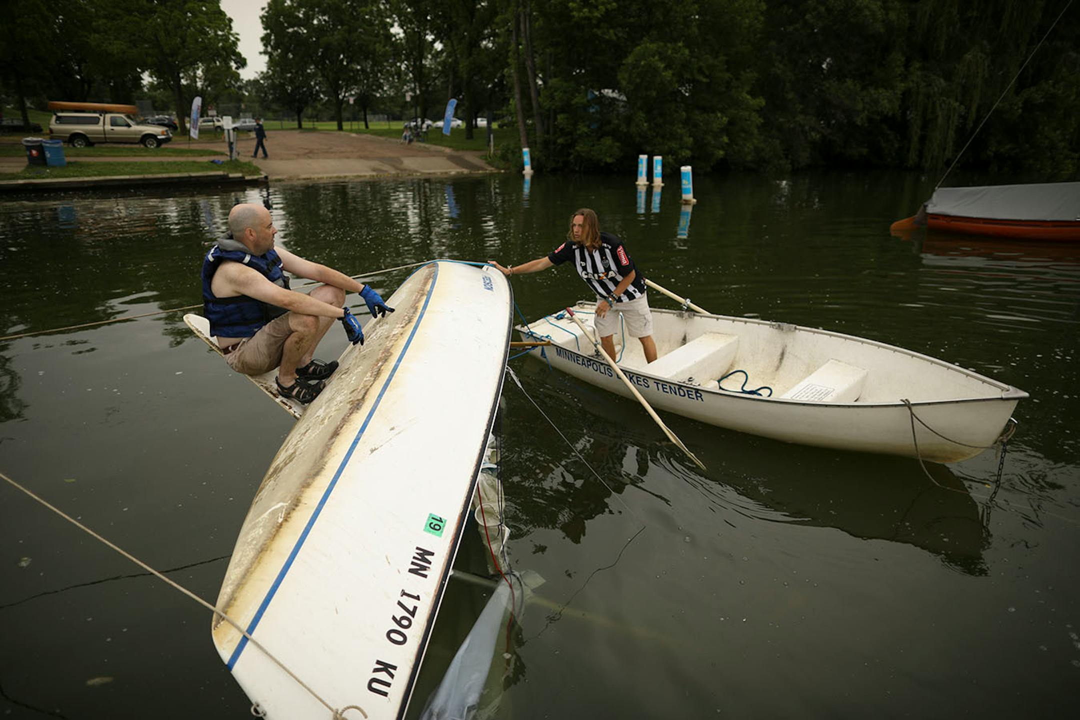 Martin Conroy sat on the keel of his boat while Isaac Fuglestad got ready to try to free the mast from the lake bottom as they attempted to right his overturned sailboat on Lake Nokomis Sunday afternoon. When he drove past the lake after the storm Sunday morning, "I saw that I was the only one flipped, so I went home and changed for my unplanned afternoon adventure."