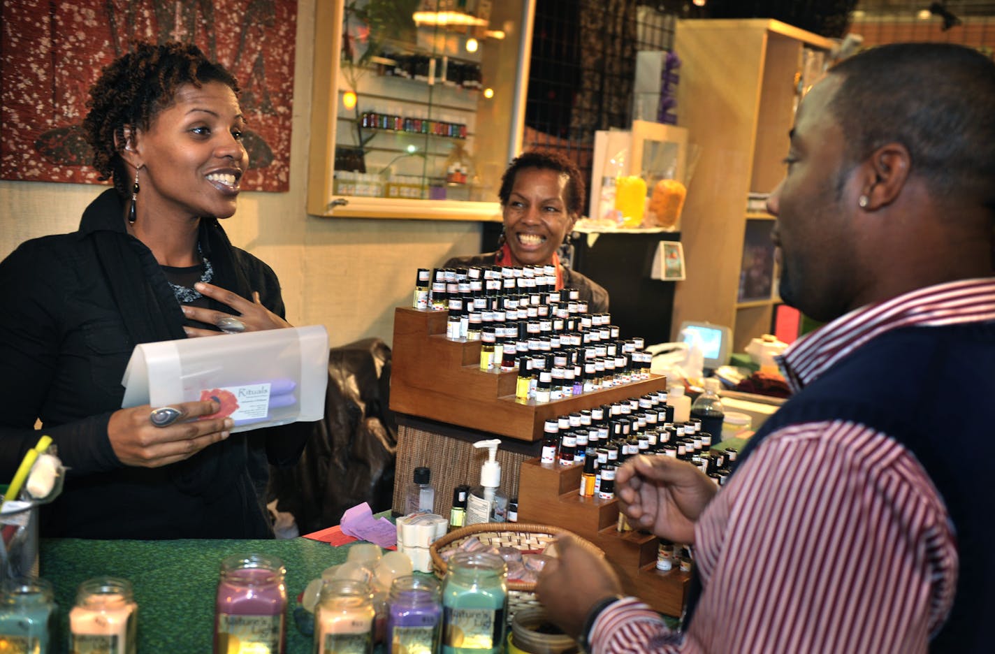 Mai'sah Blanton, left, and her mother, Antoinette Williams, center, sang "Happy Birthday" to customer Montrell Pouncy last week at Rituals, their gift shop in the Midtown Global Market. Rituals and the Global Market are seeing better times as year-over-year sales increase.