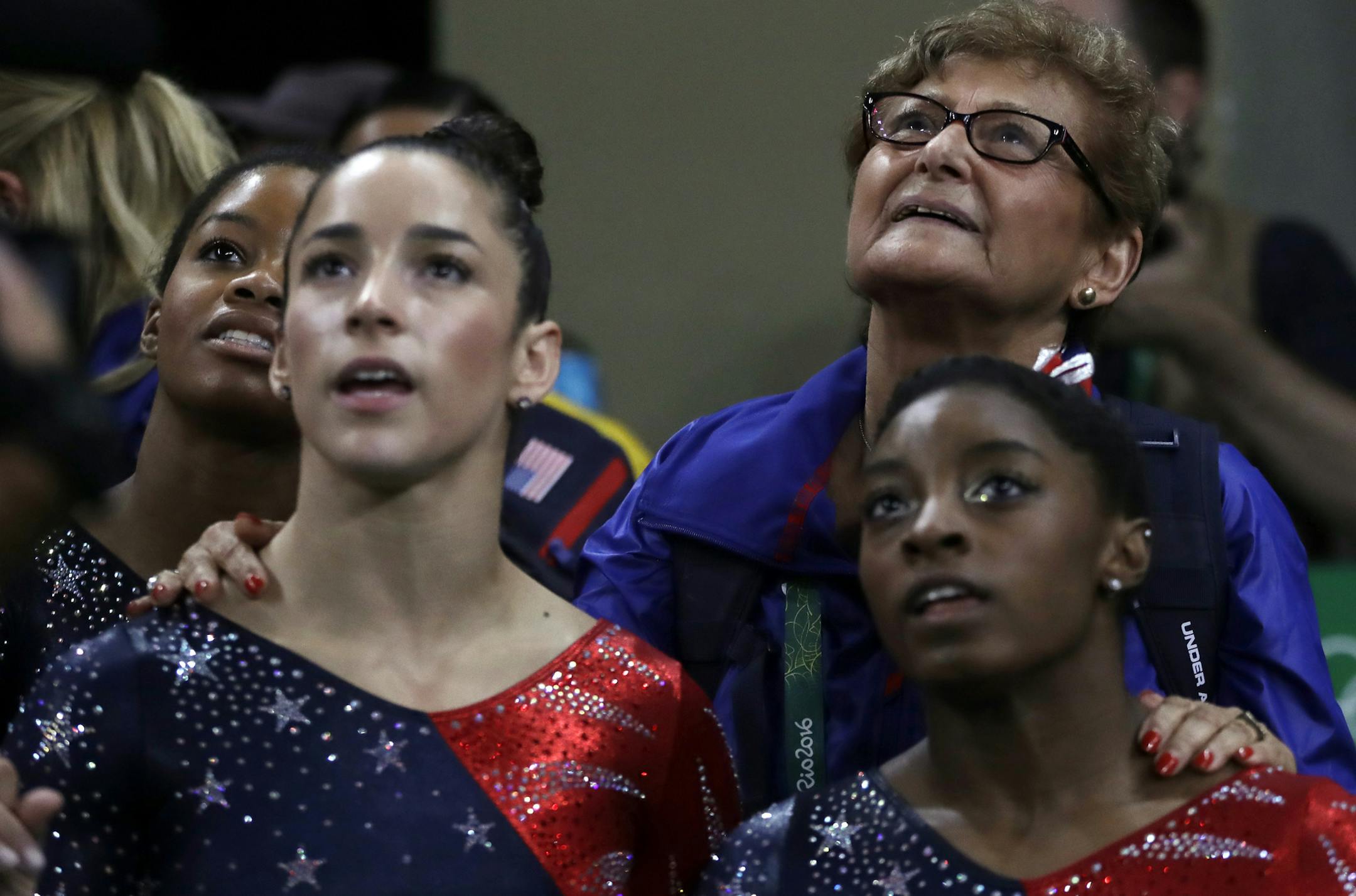 Marta Karolyi, U.S. gymnastics team coordinator, looks at the scoreboard along with, from right, Simone Biles, Aly Raisman and Gabrielle Douglas during the artistic gymnastics women's qualification at the 2016 Summer Olympics in Rio de Janeiro, Brazil, Sunday, Aug. 7, 2016. (AP Photo/Julio Cortez)