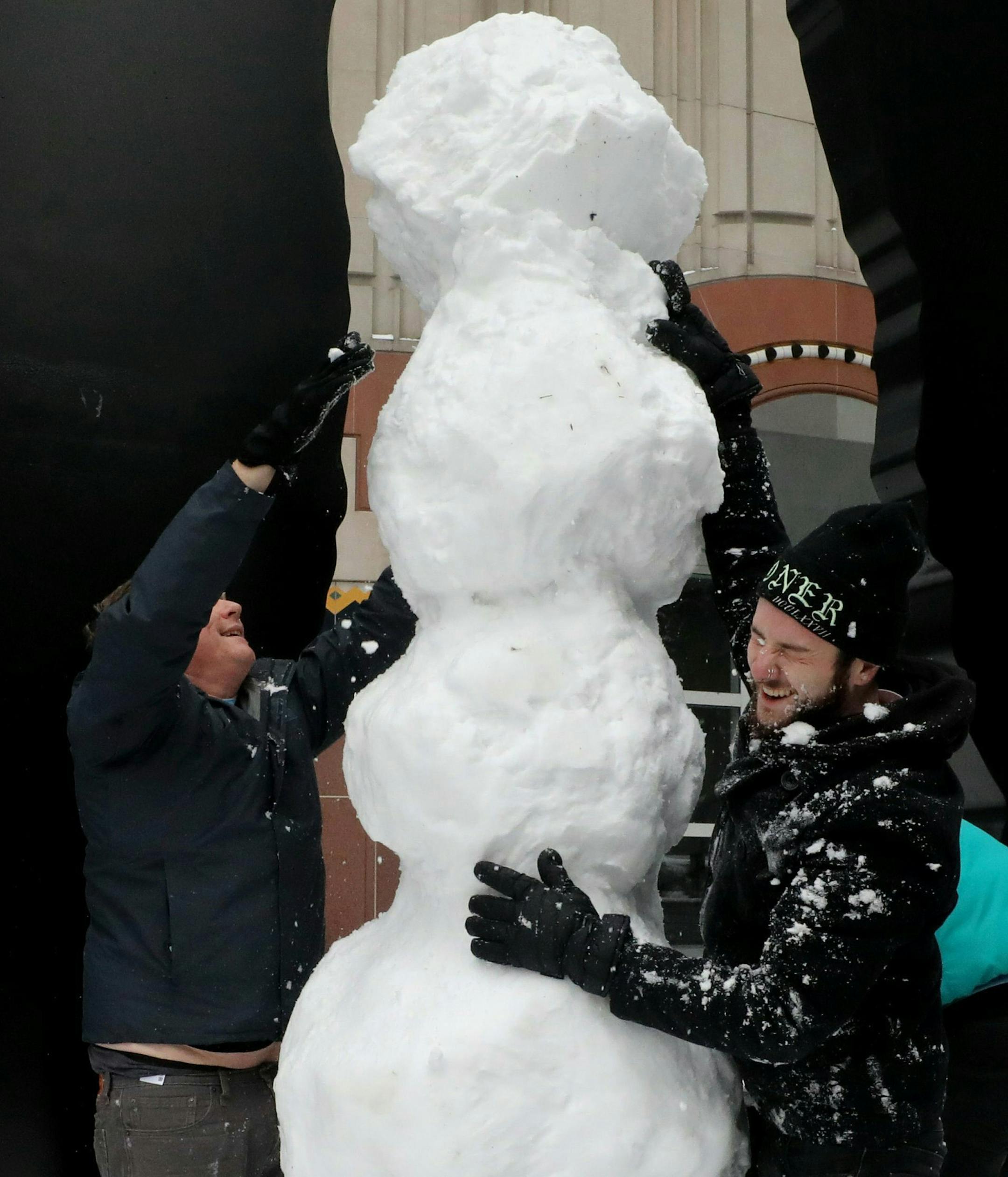 It's a tall order as Michael Delbridge, left, Dre Spliffman and three other friends gathering more material construct a snowman beneath Hammering Man in front of the Seattle Art Museum Saturday, Feb 9, 2019, in Seattle. Residents of the Pacific Northwest took to neighborhood hills with skis, sleds or even just laundry baskets Saturday to celebrate an unusual dump of snow in a region more accustomed to winter rain. (Alan Berner/The Seattle Times via AP)