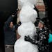 It's a tall order as Michael Delbridge, left, Dre Spliffman and three other friends gathering more material construct a snowman beneath Hammering Man 