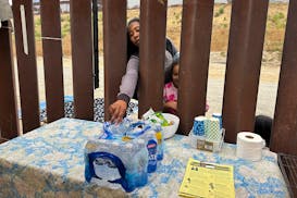 A woman seeking asylum reaches for a bottle of water after crossing the border with a child on June 5 in San Diego, Calif. President Joe Biden has unv