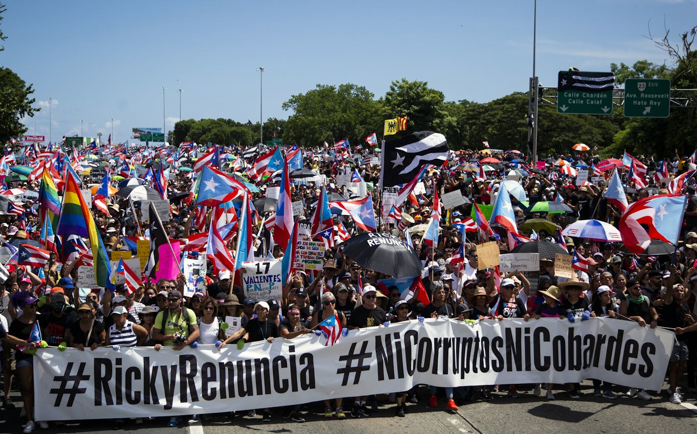 Demonstrators hold a banner reading "Ricky resign" and "Neither corruption nor cowards" as they gather on Highway 18, also known as Expreso Las Am&#xe9;ricas, in San Juan, Puerto Rico, on Monday, July 22, 2019. Tens of thousands of Puerto Ricans filled miles of the major highway on Monday to march in what appears to be one of the largest protests the island has ever seen against Rossell&#xf3;, who has resisted persistent calls for his resignation. (Erika P. Rodriguez/The New York Times)