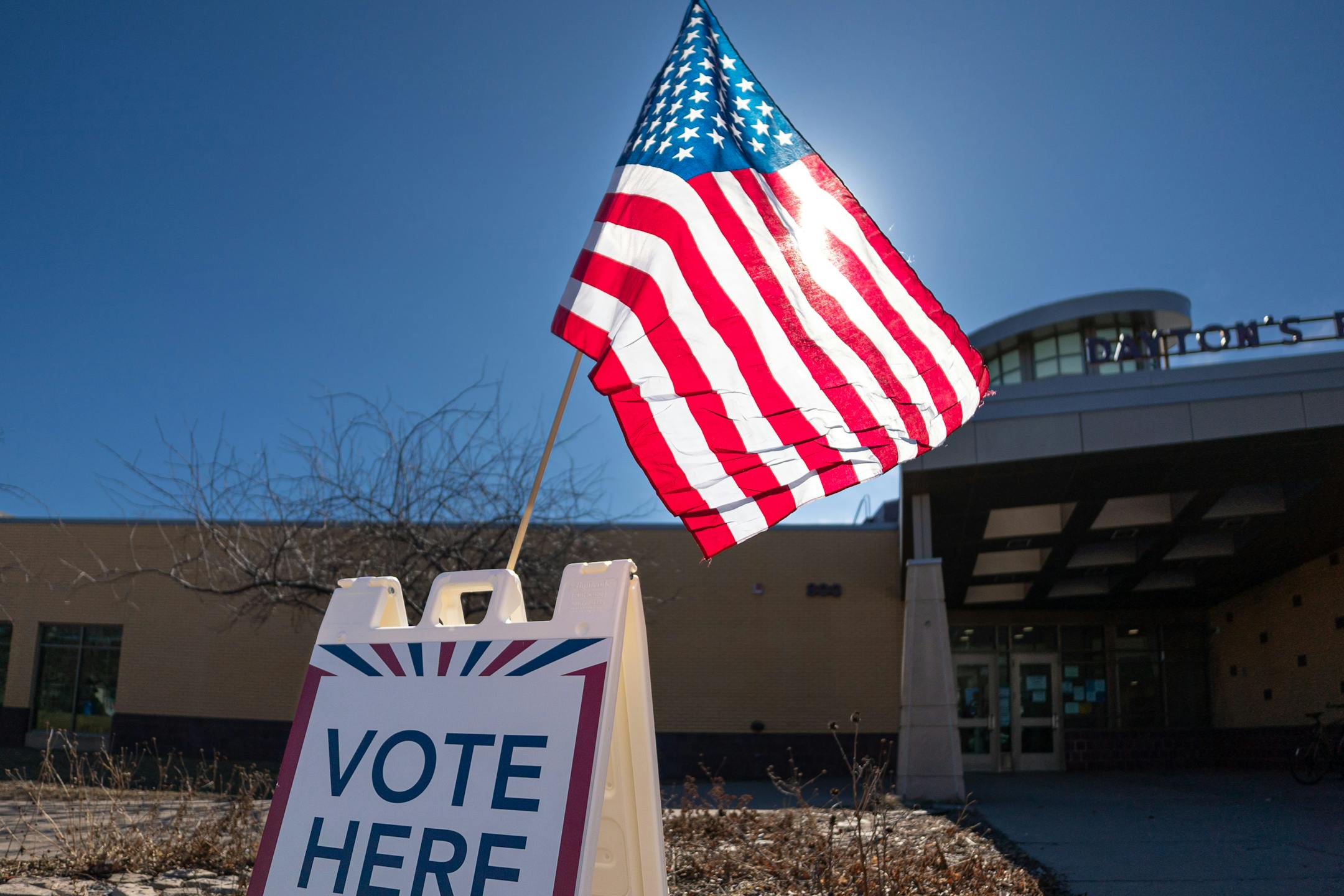 A sign says "vote here" outside a polling place entrance in St. Paul with an American flag above it.