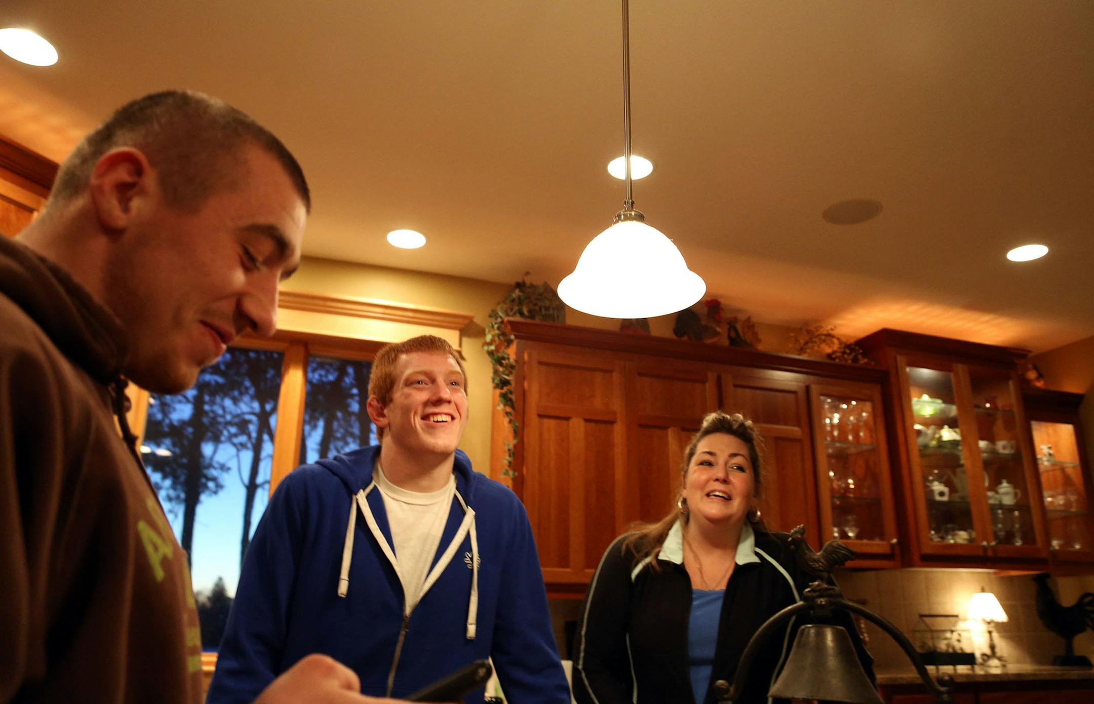 Luke Benick, left, brother Lance and mother Joanne laughed in the family kitchen in Scandia, Minn., after looking at a picture of Lance being pinned by his father, Tom. Joanne Benick is battling a brain tumor. Lance Benick, a Totino-Grace junior, is 30-0 this season.