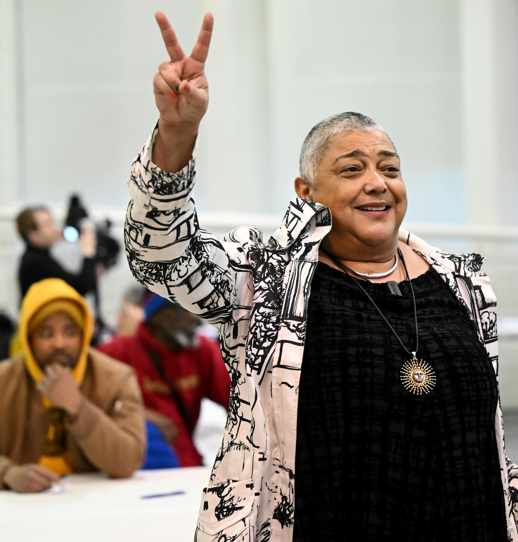 Marnita Schroedl gives the peace gesture as she spoke to attendees of a gathering. Schroedl, and her organization Marnita's Table, are co-hosting the night's event.