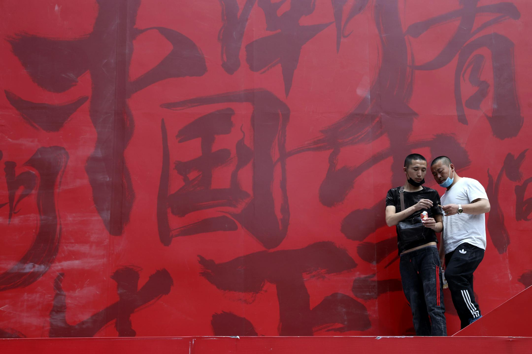Workers share cigarettes near a booth promoting Made in China with Chinese calligraphy for "China Trendy" in Beijing on Wednesday, May 8, 2019. China's exports fell in April amid a punishing tariff war with Washington, adding to pressure on Beijing on the eve of negotiations aimed at settling the fight over its technology ambitions. (AP Photo/Ng Han Guan)