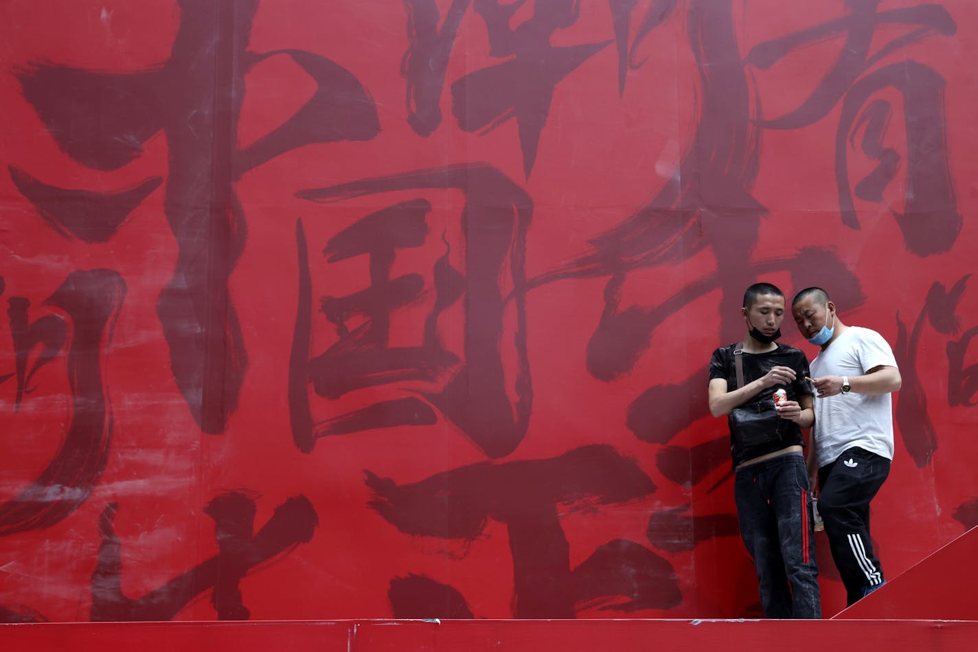 Workers share cigarettes near a booth promoting Made in China with Chinese calligraphy for "China Trendy" in Beijing on Wednesday, May 8, 2019. China's exports fell in April amid a punishing tariff war with Washington, adding to pressure on Beijing on the eve of negotiations aimed at settling the fight over its technology ambitions. (AP Photo/Ng Han Guan)