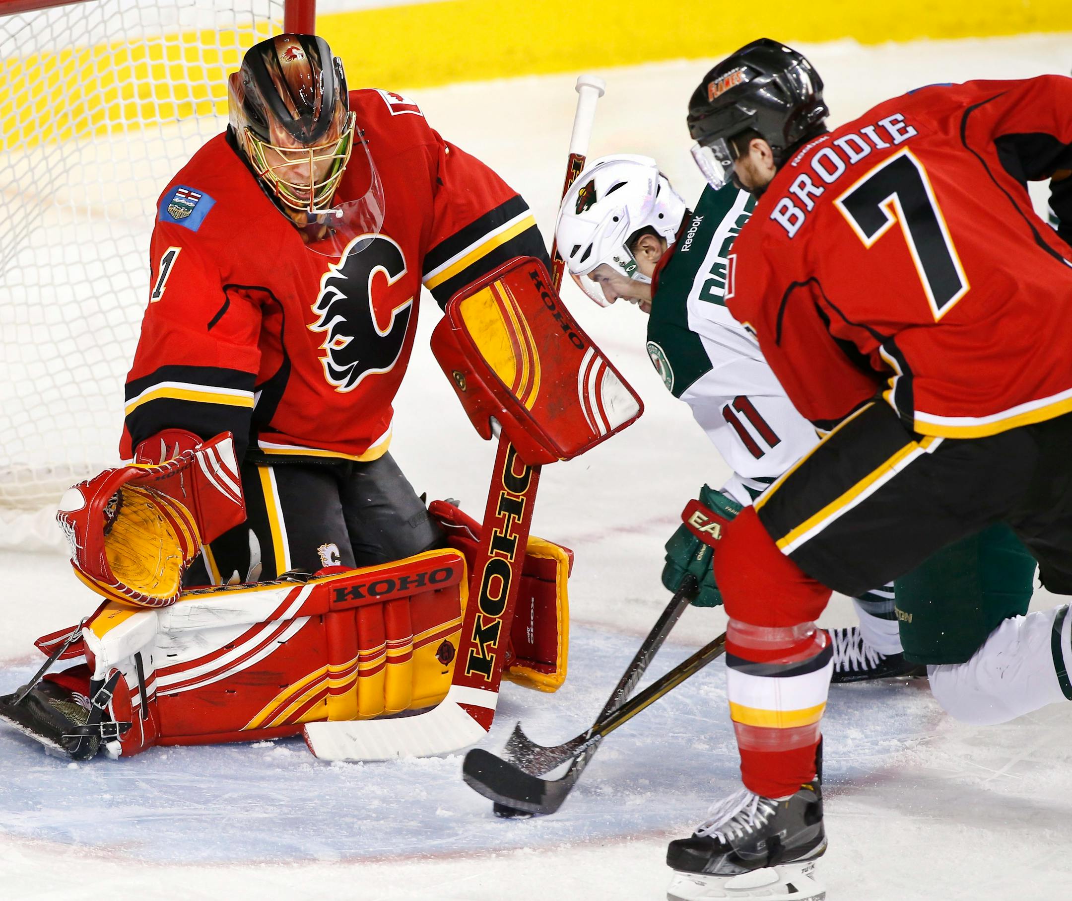 Minnesota Wild's Zach Parise (11) battles for the puck with Calgary Flames' TJ Brodie in front of Calgary goalie Jonas Hiller, from Switzerland, during the second period of an NHL hockey game Wednesday, Feb. 17, 2016, in Calgary, Alberta. (Larry MacDougal/The Canadian Press via AP)