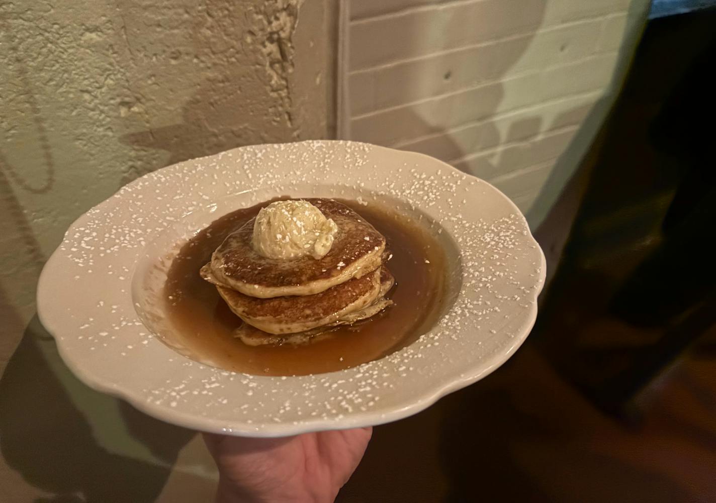 Four small pancakes in a pool of syrup with a scoop of butter on top.