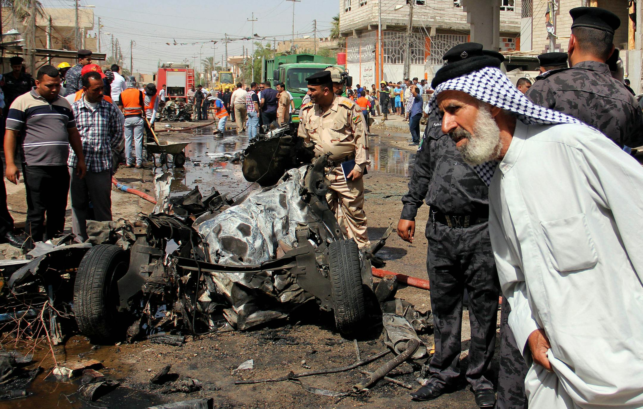 An Iraqi man and Iraqi security force members inspect the site of a car bomb attack in Basra, 340 miles (550 kilometers) southeast of Baghdad, Iraq, Sunday, June 16, 2013. Most of the car bombs hit Shiite-majority areas and were the cause of most of the casualties. The blasts hit half a dozen cities and towns in the south and center of the country. (AP Photo/Nabil al-Jurani)