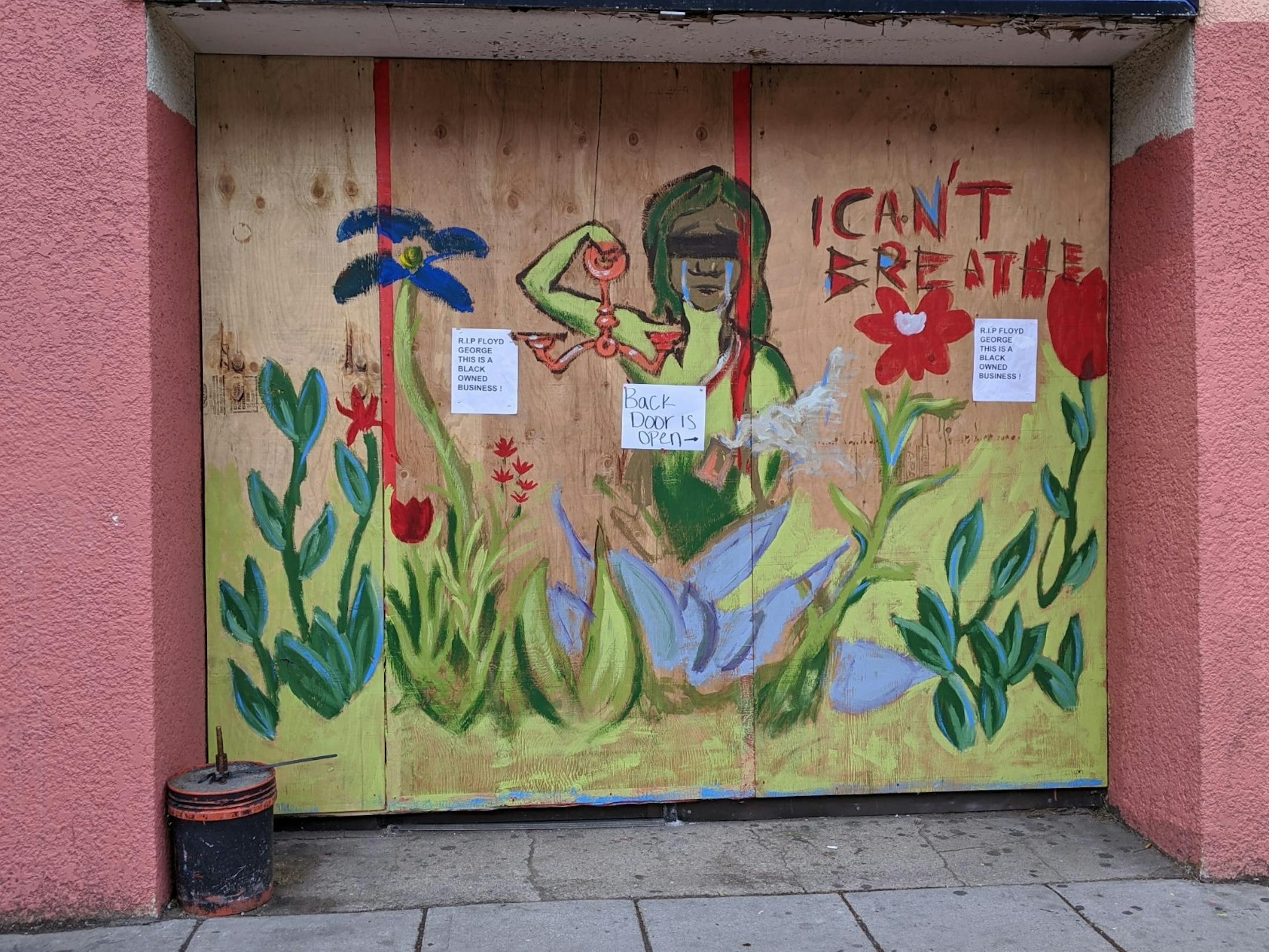 A crying, mermaid-like character with a line of black over its eyes holds an empty scale of justice in an imagined green garden on a mural at Lake Street Chiropractic (1518 E Lake St.).
