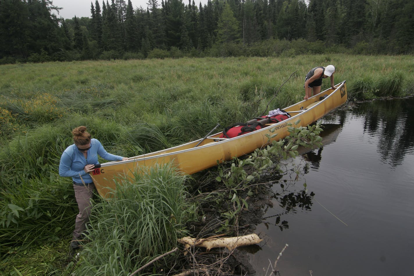 Sisters Kelly and Megan Smith slid their laden canoe over a beaver dam during a trek into the BWCA last week.