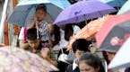 A Thai boy, carried on the shoulder, holds an umbrella as pedestrians walk over overpass in the rain Bangkok, Thailand.