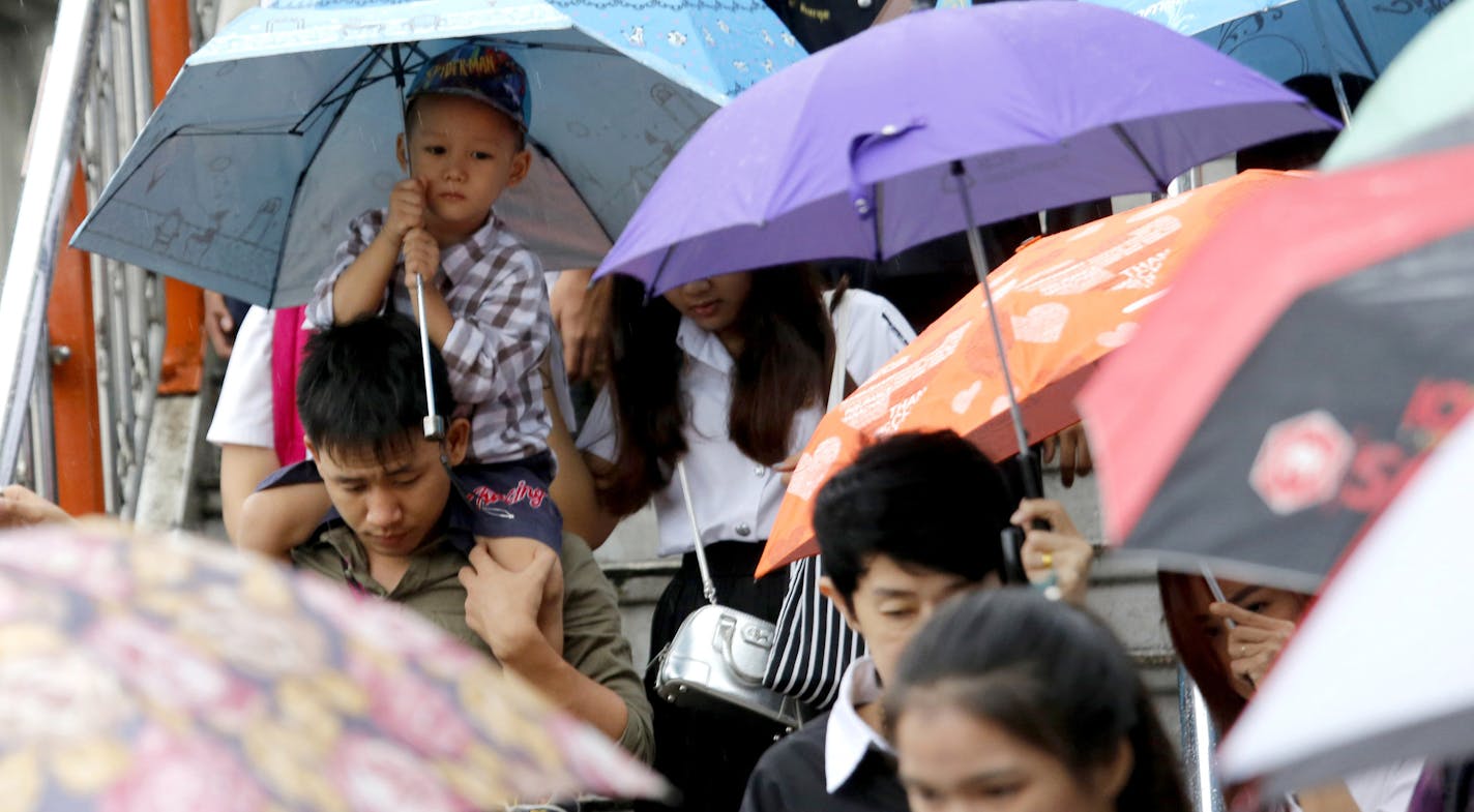 A Thai boy, carried on the shoulder, holds an umbrella as pedestrians walk over overpass in the rain Bangkok, Thailand.