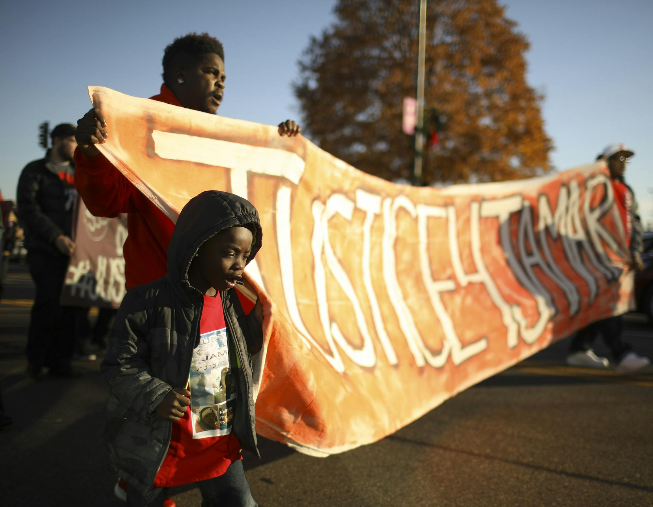 Quincy Hill and his son, Quincy Jr. helped carry a banner as people began marching west on Broadway Ave. after a gathering to remember Jamar Clark's death Sunday afterrnoon. Both are cousins of Clark. ] JEFF WHEELER ï jeff.wheeler@startribune.com A week of events began Sunday, November 13, 2016 to honor Jamar Clark, who was killed by Minneapolis Police a year ago Tuesday. About 75 people gathered in the Cub Foods parking lot on Broadway Ave. and after listening to a few speakers, including