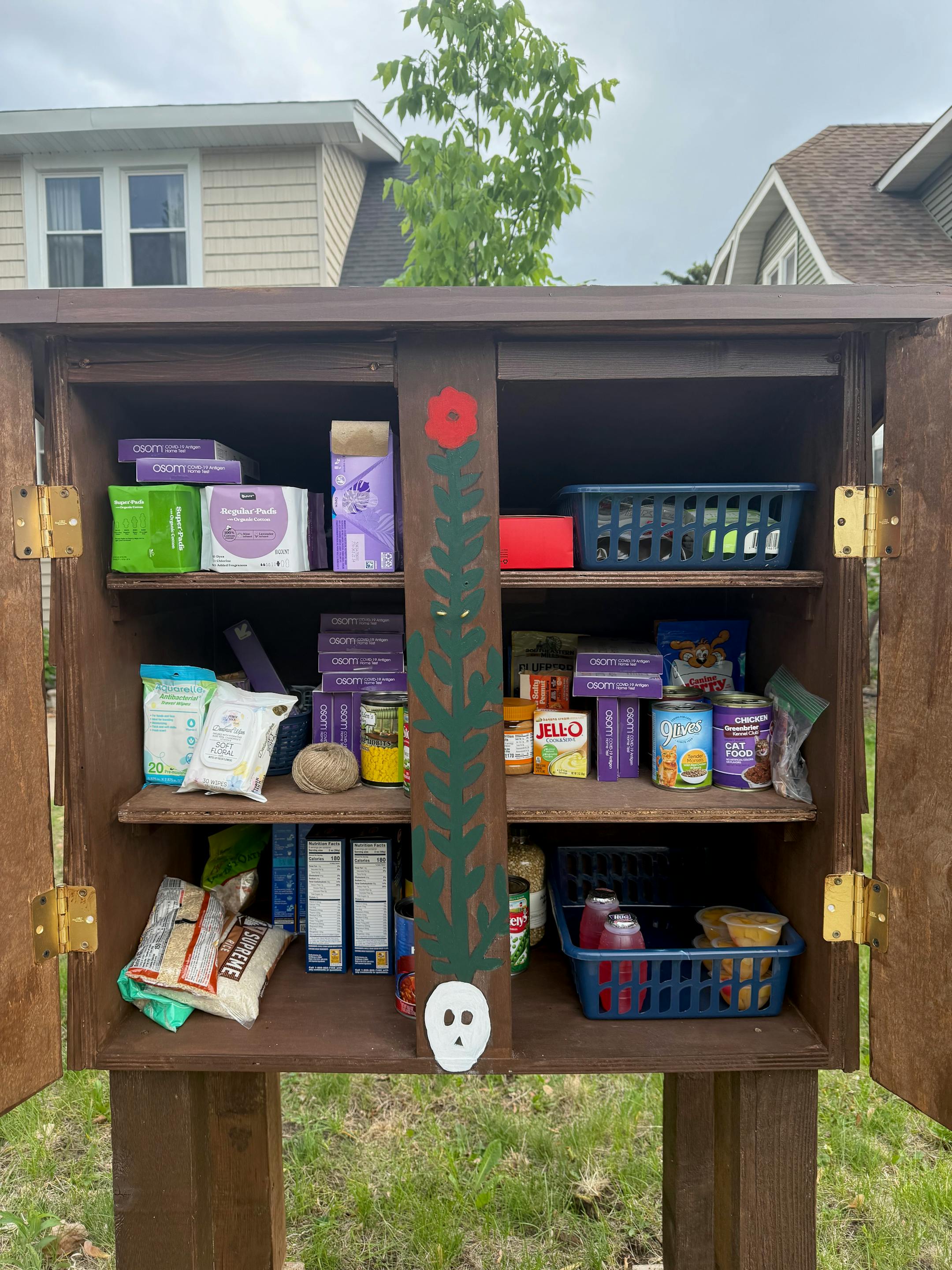 A wooden pantry with the doors open reveals three shelves of food-shelf items.