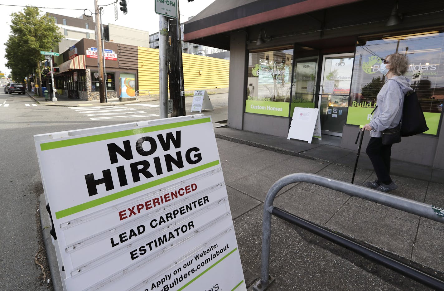 In this photo taken Thursday, June 4, 2020, a pedestrian wearing a mask walks past reader board advertising a job opening for a remodeling company, in Seattle. The U.S. unemployment rate fell to 13.3% in May, and 2.5 million jobs were added — a surprisingly positive reading in the midst of a recession that has paralyzed the economy and depressed the job market in the wake of the viral pandemic. (AP Photo/Elaine Thompson)