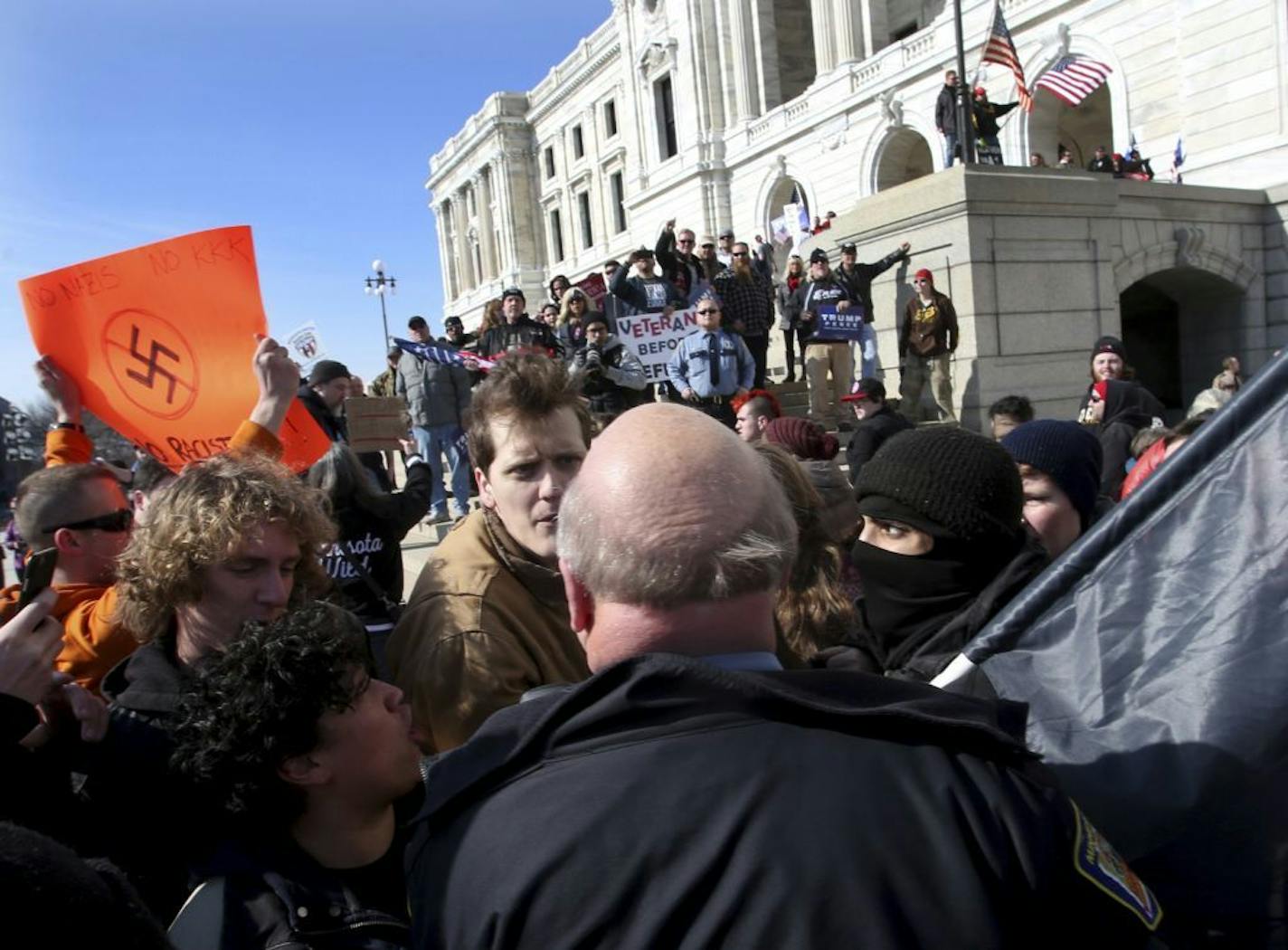 As a crowd of President Donald Trump supporters watch from atop the steps a police officer approaches anti-Trump protesters outside the State Capitol during a national March 4 Trump at the State Capitol Saturday, March 4, 2017, in St. Paul, Minn.