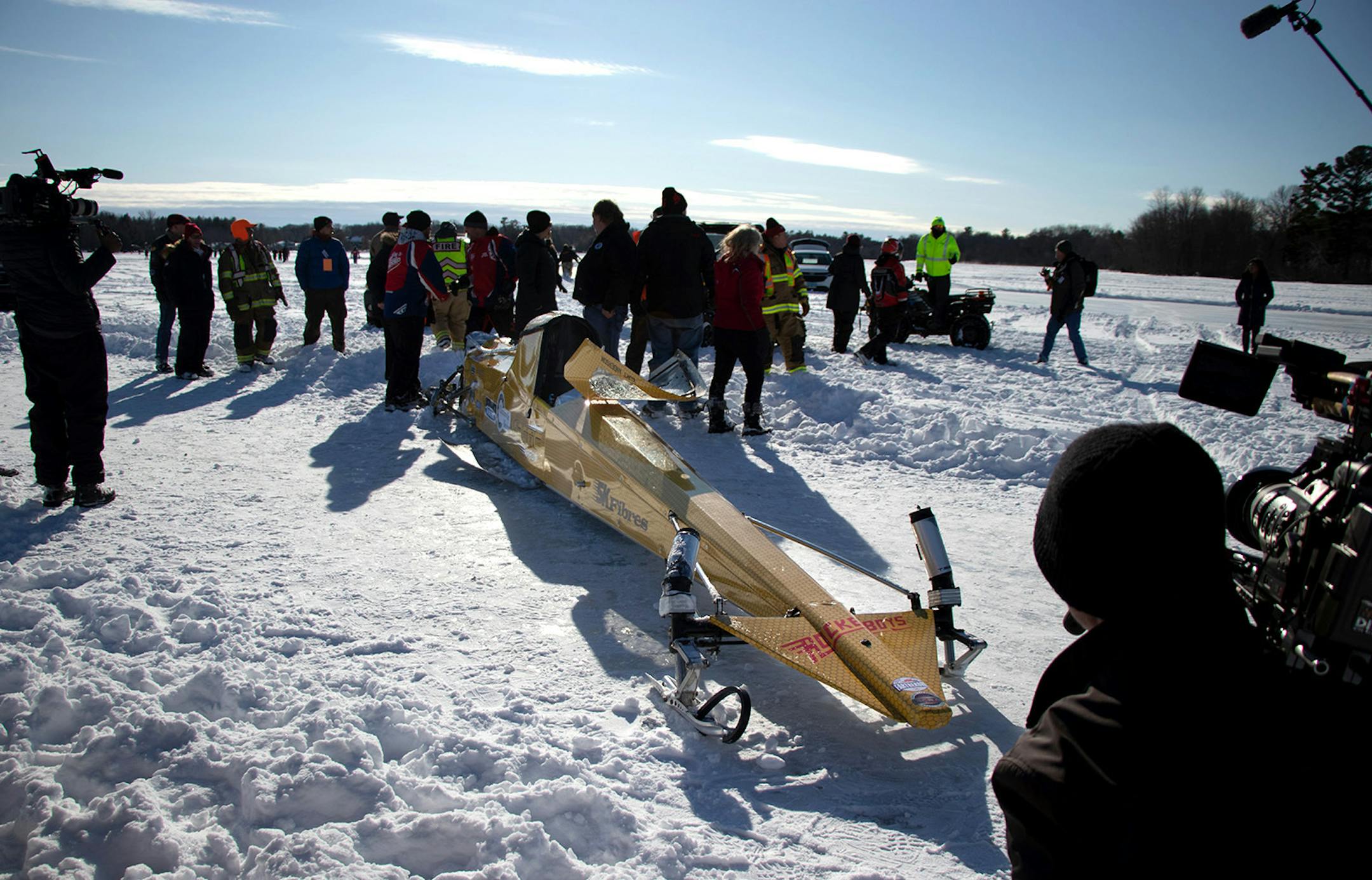 First responders, Snodeo coordinators, Rocketboys crew, the TV film crew and other media gather around the wrecked Arctic Arrow while driver Kurt Anderson is checked by medical personel after the Arrow crashed on its second run on Sunday, Feb. 16, 2020 on Bear Lake in Manawa, WI.